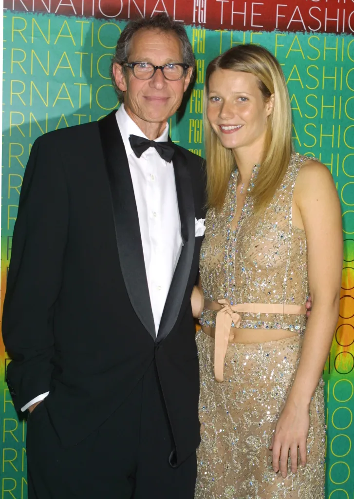 Bruce Paltrow, in a black tuxedo, and Gwyneth Paltrow, in a gold gown, posing together at an event.