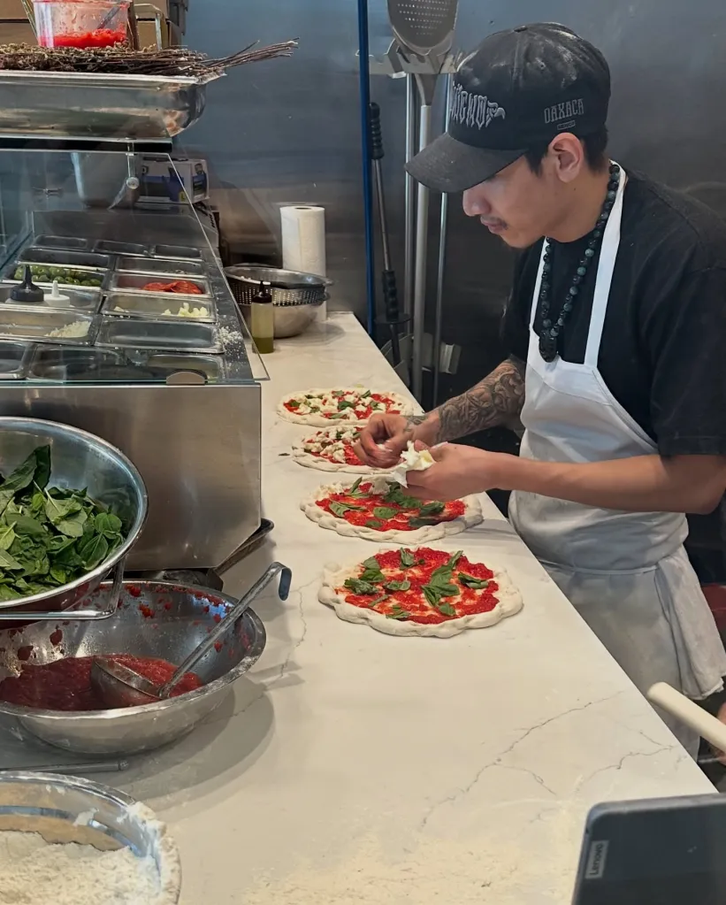 A chef preparing several pizzas in a restaurant kitchen.