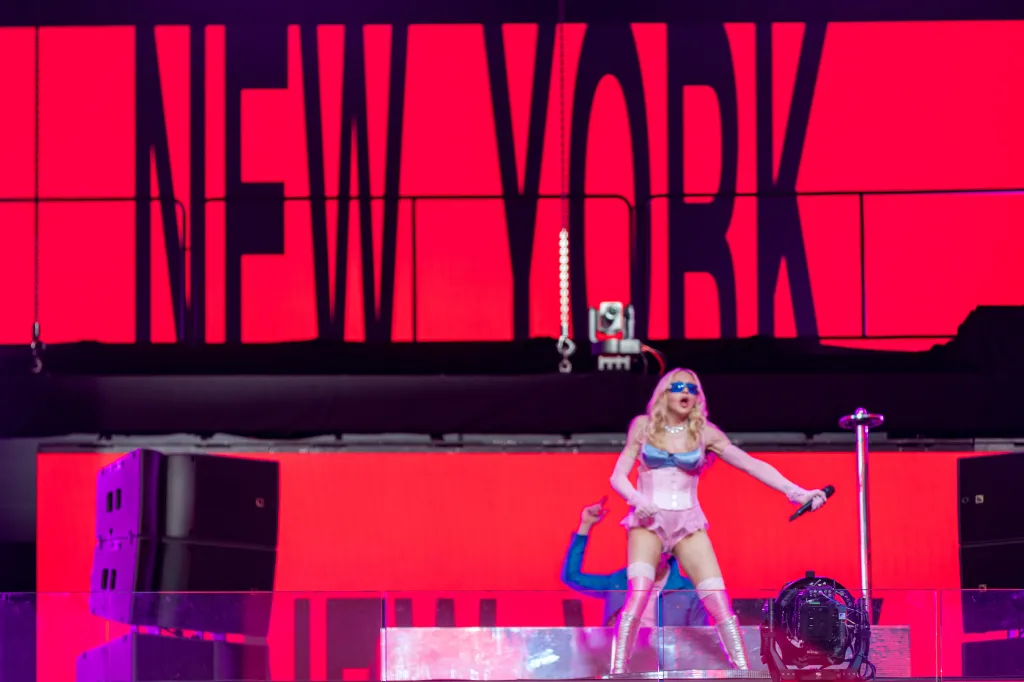 Popstar Madonna performing a pop-up concert in Times Square with a red "NEW YORK" sign in the background.