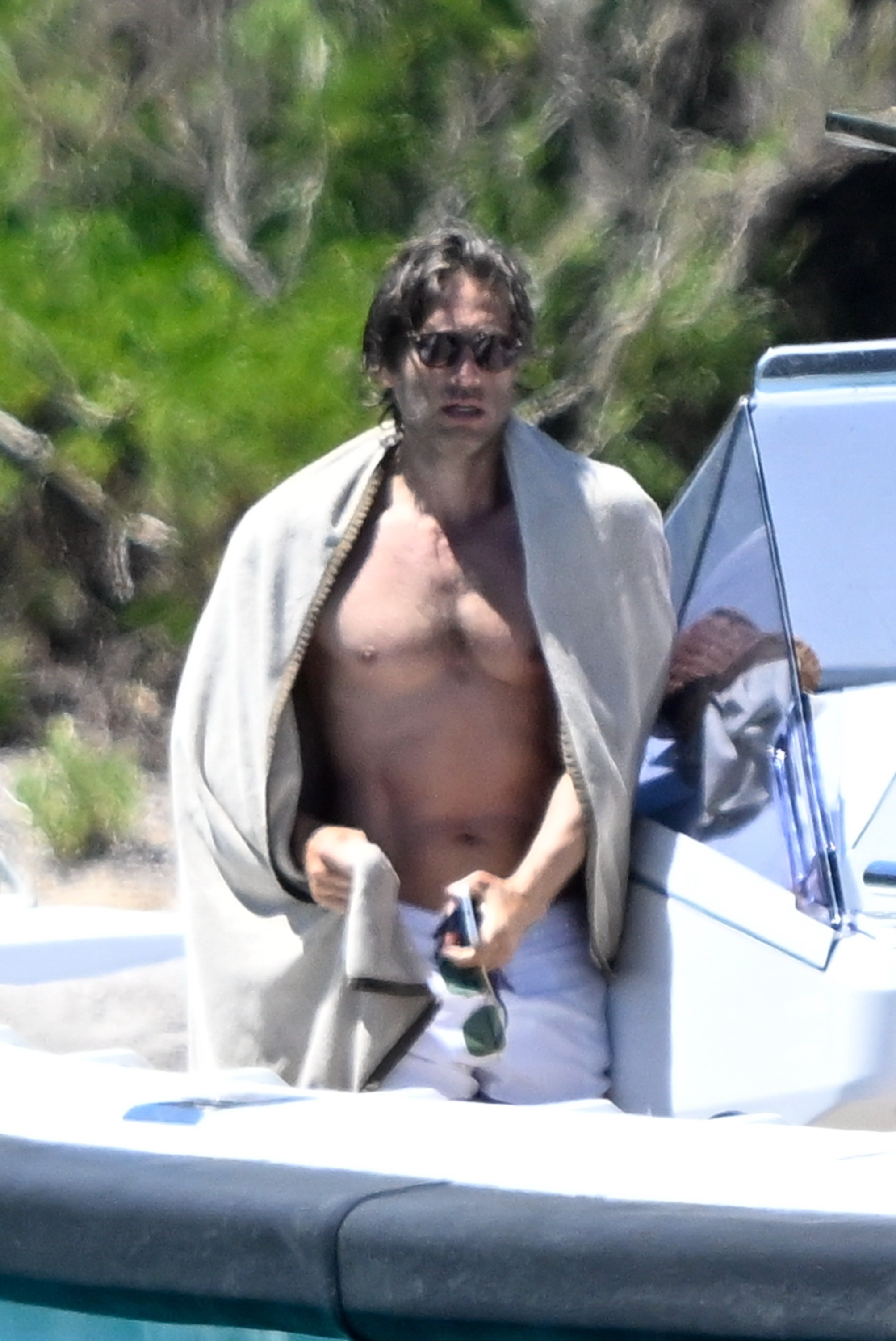Brad Falchuk on a yacht, shirtless, wearing white shorts and sunglasses, with a towel draped over his shoulders.