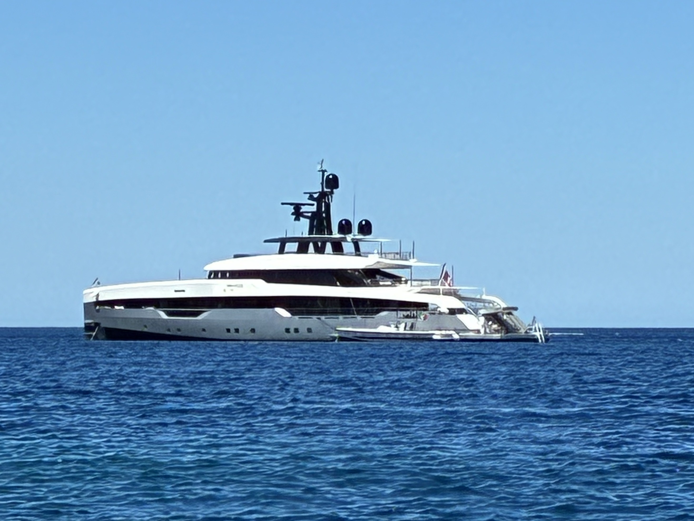 A large white superyacht at sea with clear blue skies above.