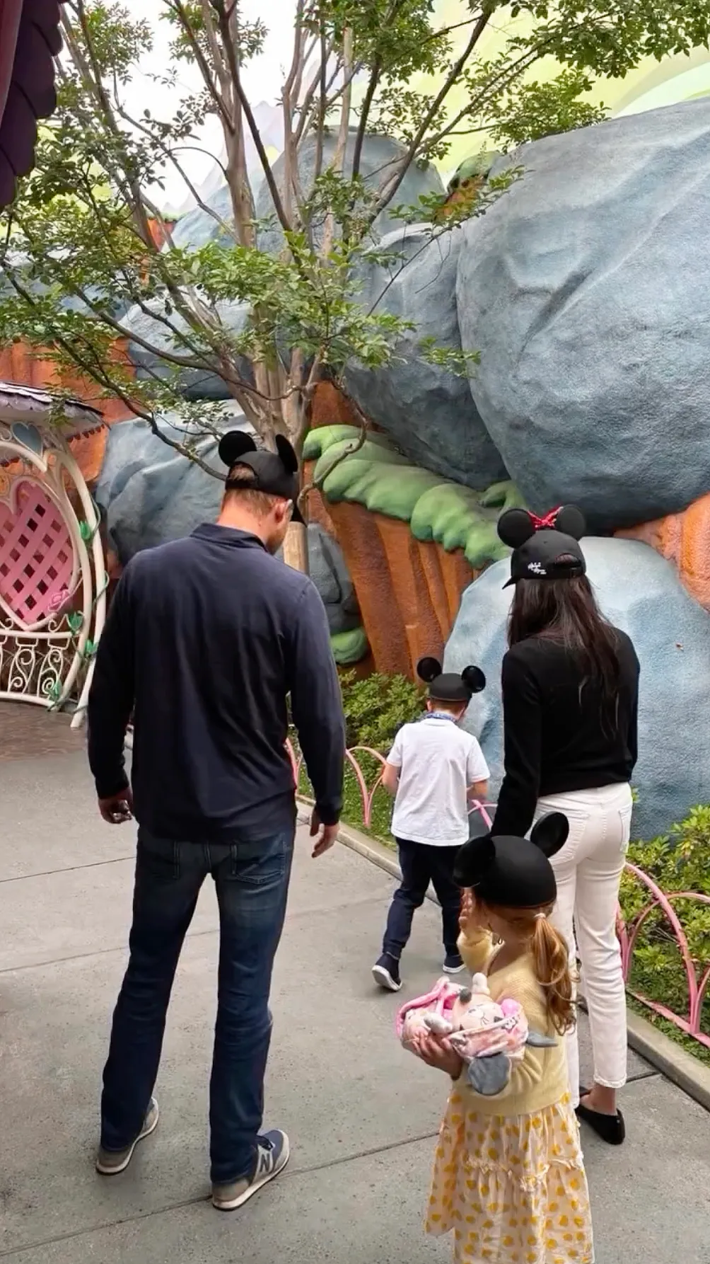 Prince Harry, Meghan Markle, Archie, and Lilibet walking away from the camera, wearing Mickey Mouse ears at Disneyland.