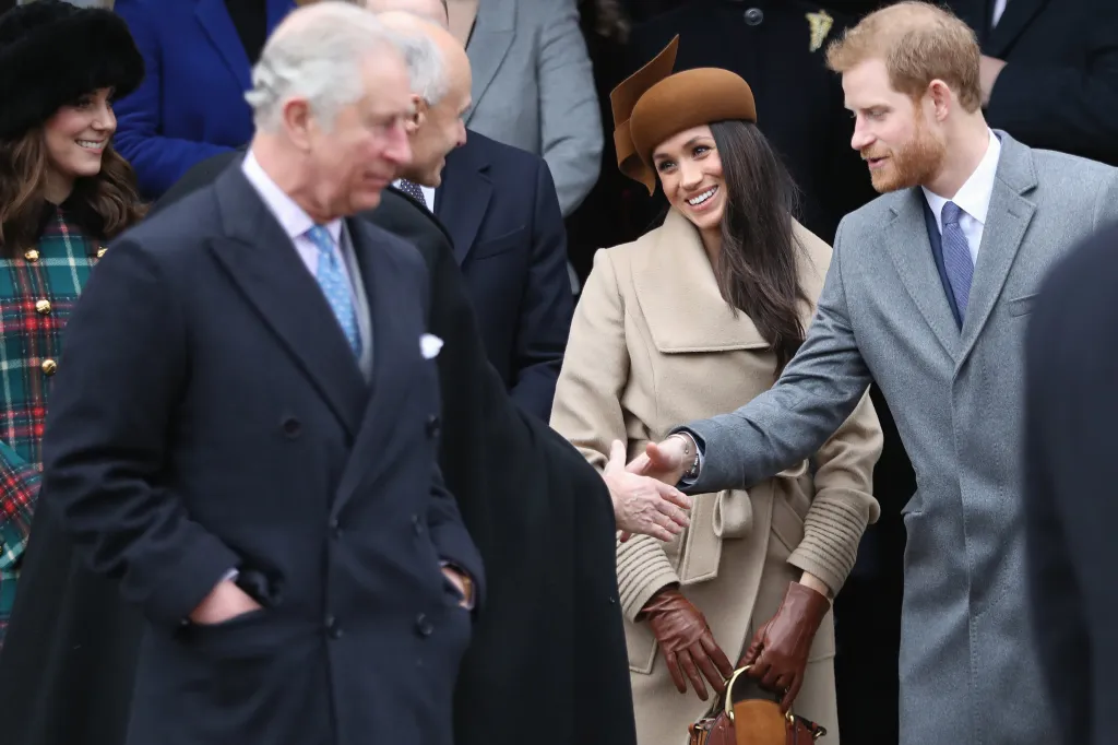 Prince Harry shaking hands with Prince Charles at a church service, with Meghan Markle smiling beside him and Catherine, Duchess of Cambridge, visible in the background.