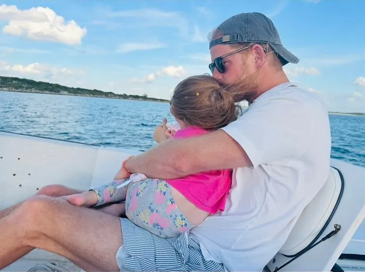 Prince Harry holding Princess Lilibet and kissing her head on a boat.