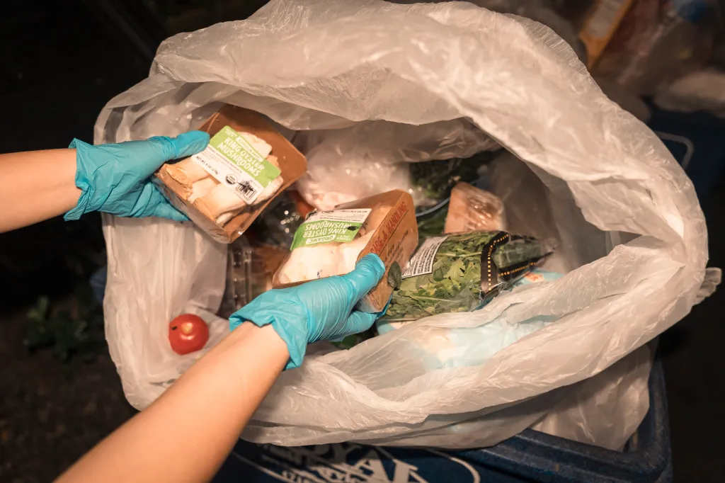 Hands pulling food from trash bag.