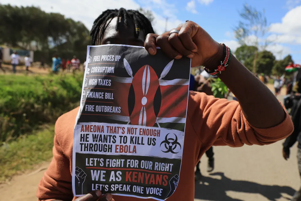 A protester holds a placard against a proposed Ebola quarantine center, listing grievances like "FUEL PRICES UP" and "CORRUPTION."