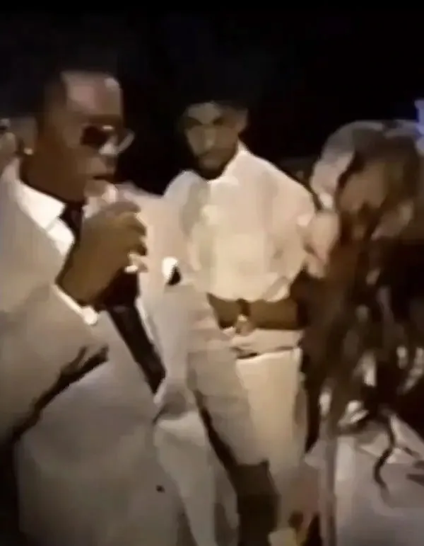 Sean "Diddy" Combs, wearing sunglasses, talks to a preteen Daveigh Chase, with another person in white behind them, backstage at an event.