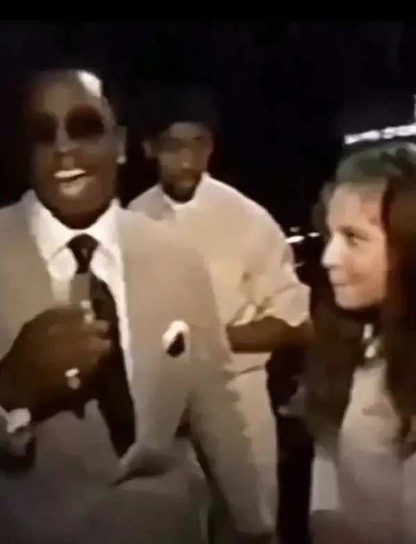 A rapper in sunglasses smiling while talking to a young actress backstage.