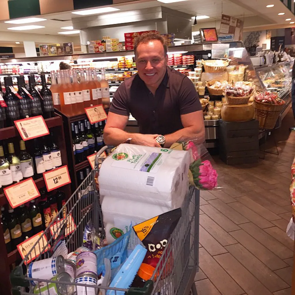 Lenny Hochstein smiling over a grocery cart full of items in a supermarket aisle.