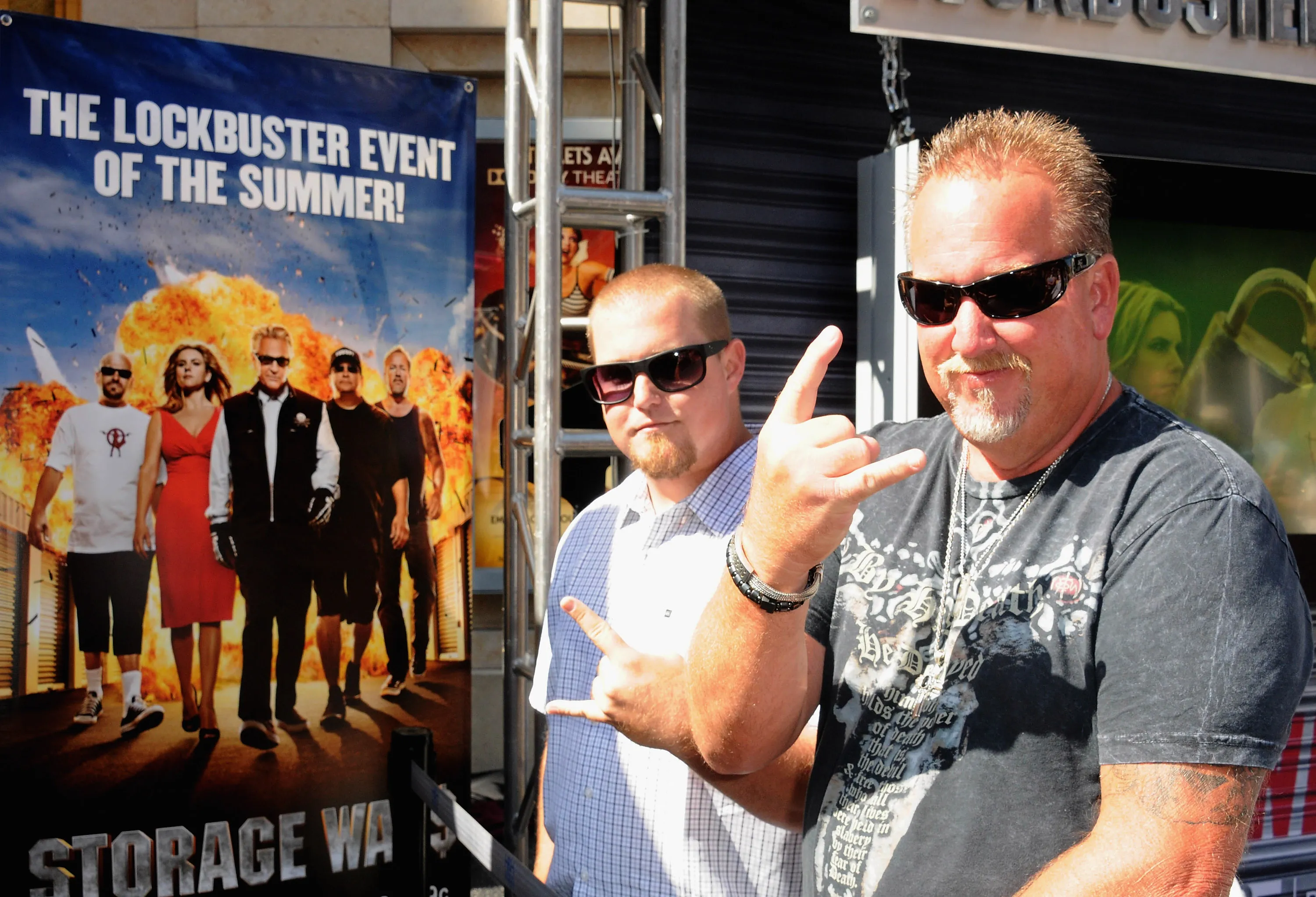 Reality stars Brandon Sheets and Darrell Sheets pose in front of a "Storage Wars" banner.
