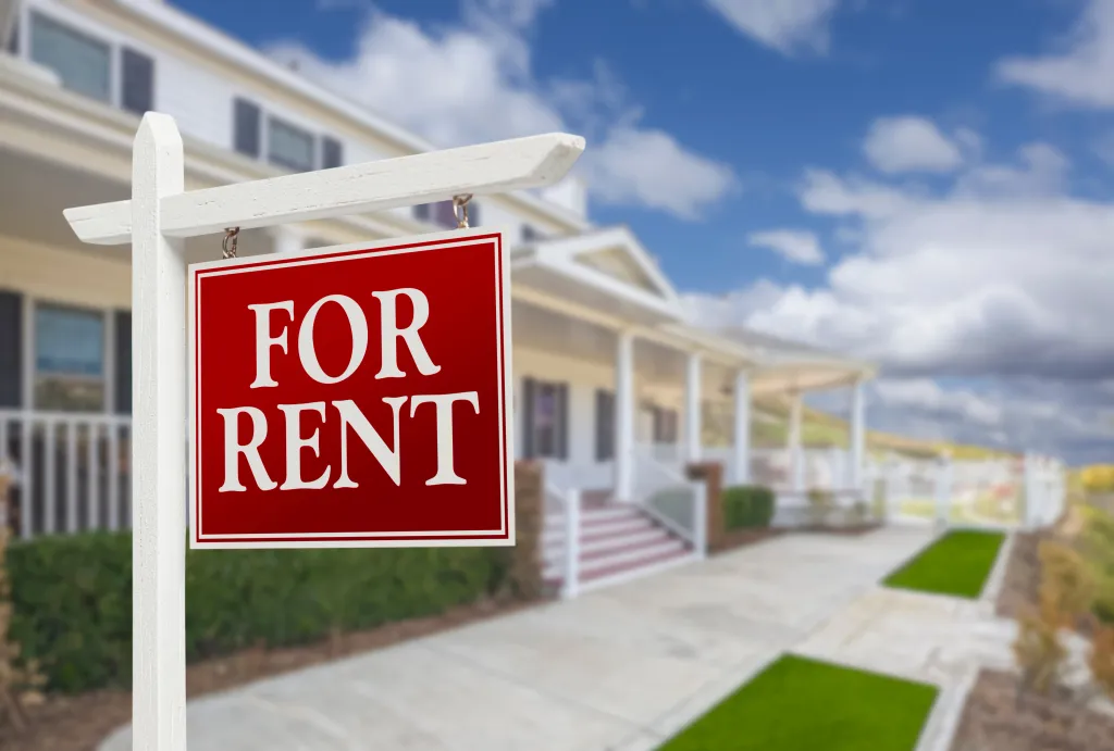 Red "FOR RENT" sign in front of a white house.