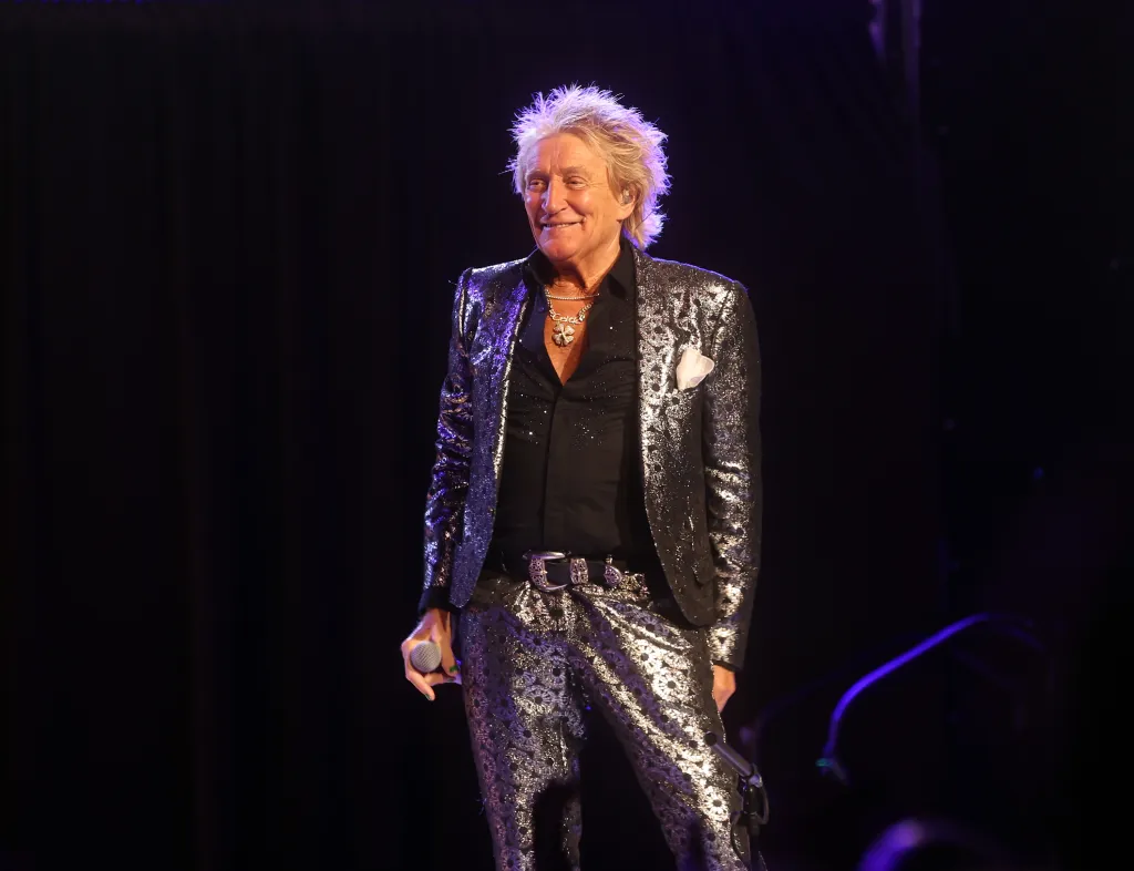 Rod Stewart performs at Mortgage Matchup Center, holding a microphone and wearing a sequined silver suit.
