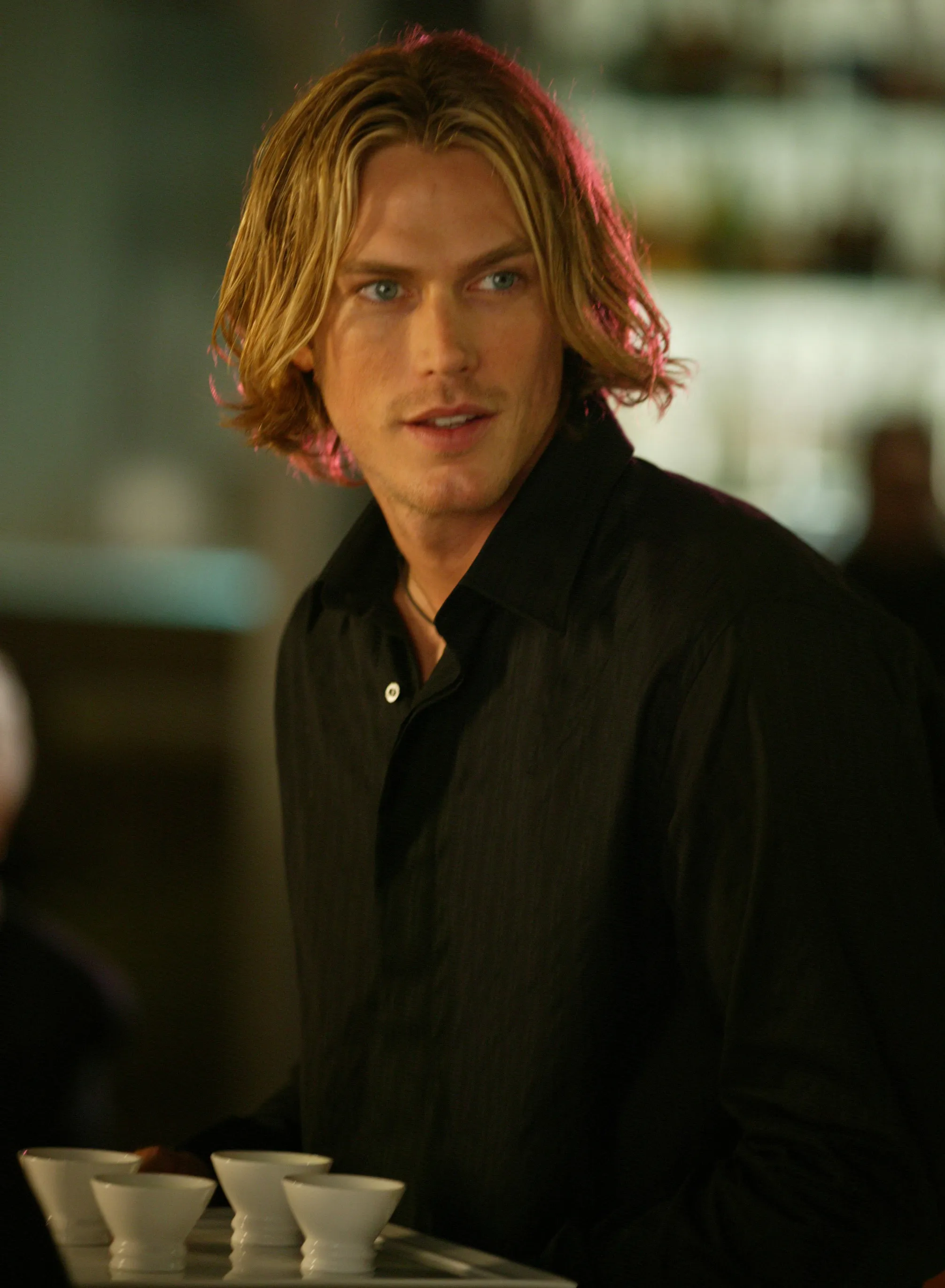 Jason Lewis as Smith Jerrod in "Sex and the City," wearing a black button-up shirt and holding a tray of drinks.