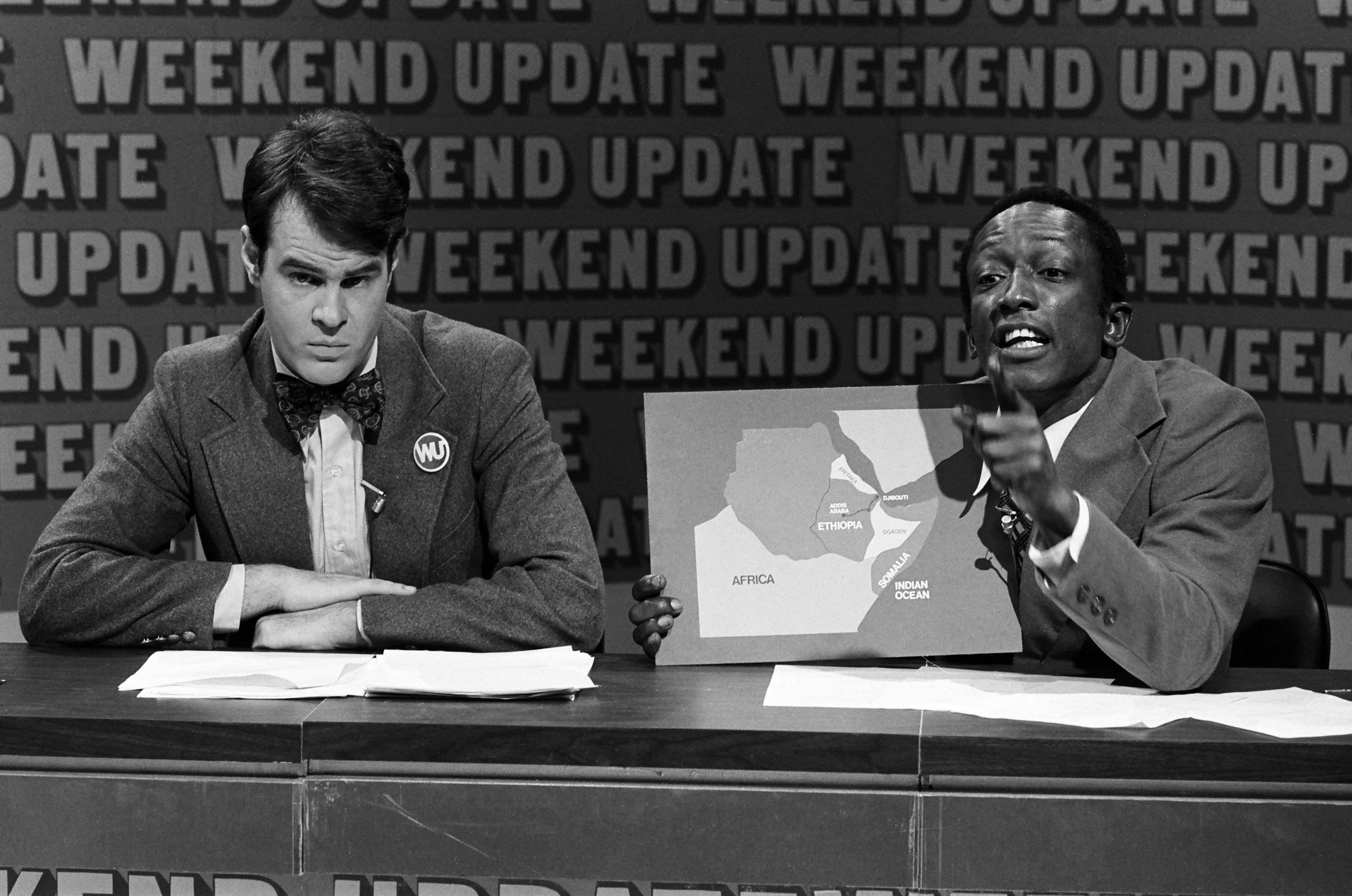 Dan Aykroyd and Garrett Morris presenting the "Weekend Update" skit, with Morris holding a map of Africa.