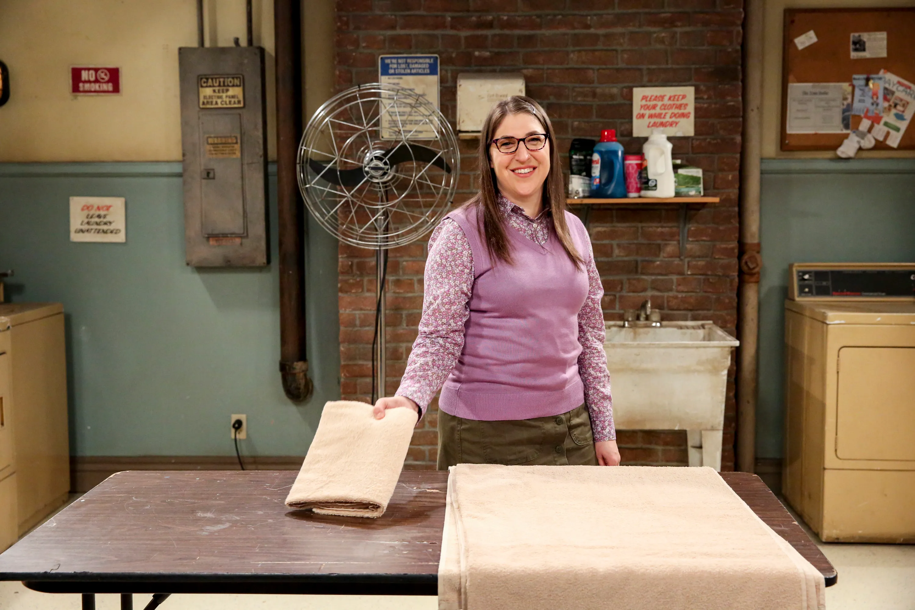 Amy Farrah Fowler in a laundry room, folding towels.