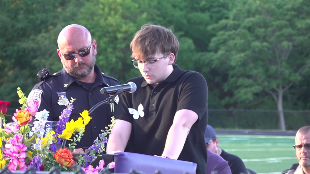 Jonathan McFarland speaking at a vigil with a police officer behind him.