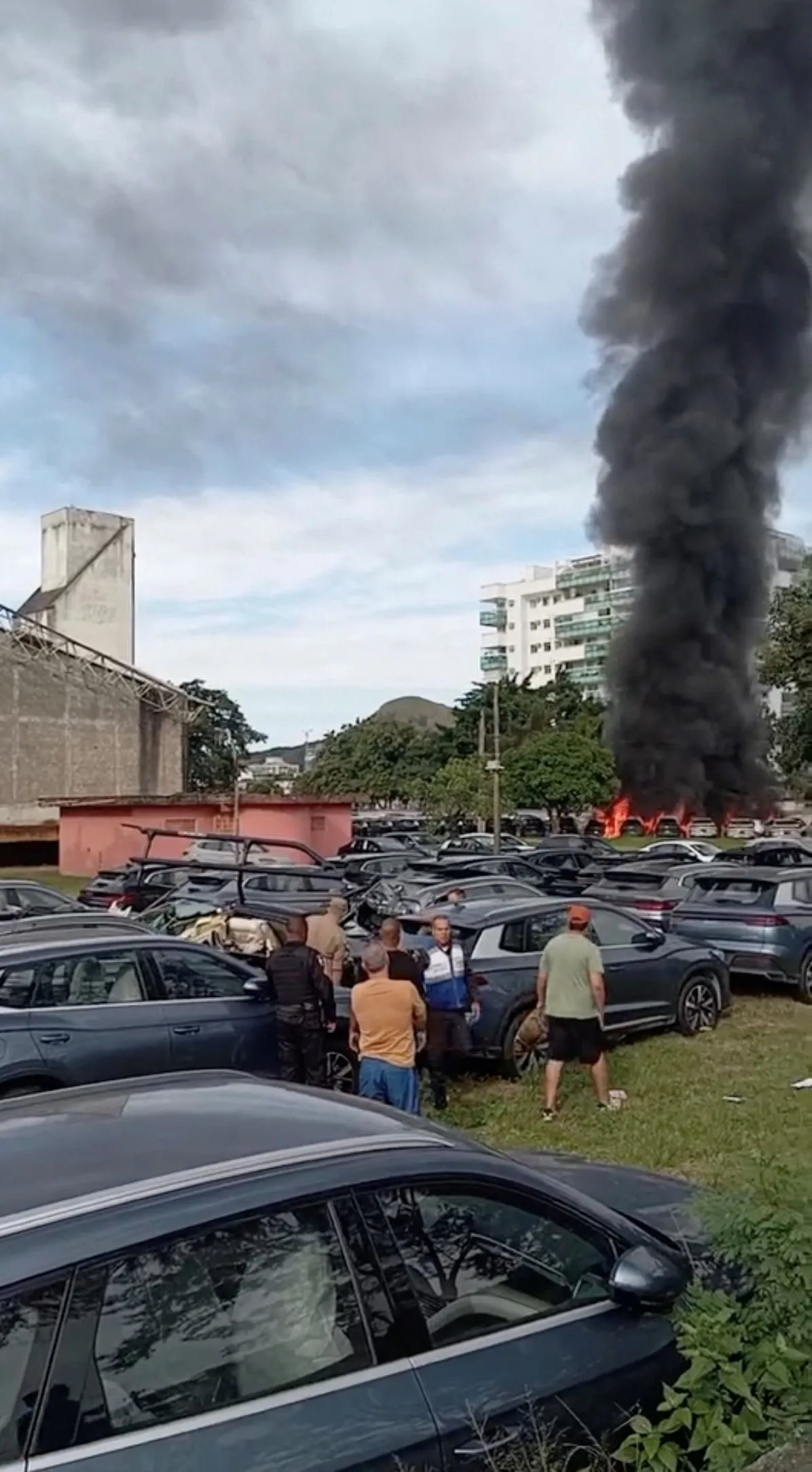 People gather in a parking lot as a thick column of black smoke rises from a fire in Rio de Janeiro after two helicopters collided.