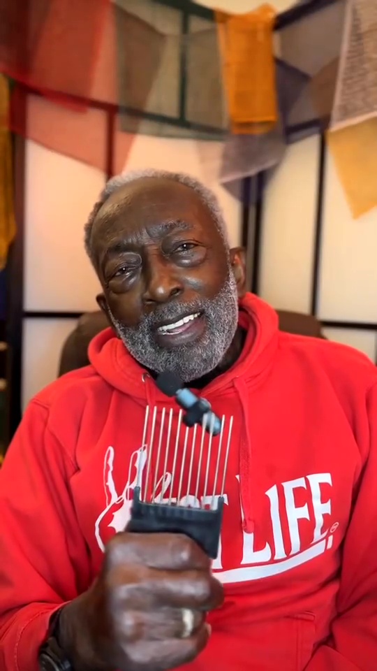Garrett Morris in a red hoodie holding an afro pick.
