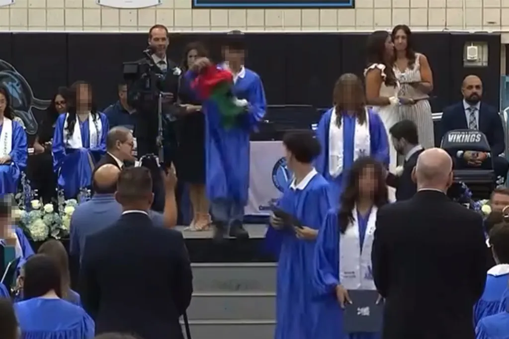 A middle schooler in a blue graduation gown waves a Palestinian flag while walking across a stage at Elias Bernstein Intermediate School 7 graduation