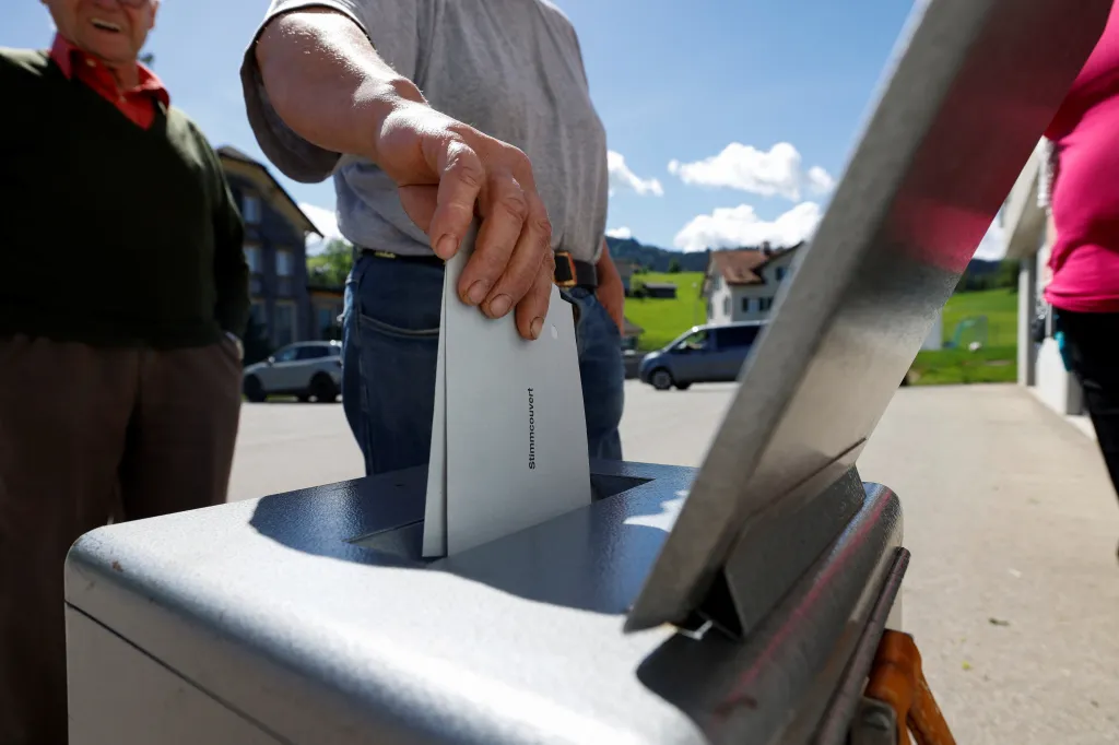 A person placing a ballot labeled "Stimmcouvert" into a ballot box.