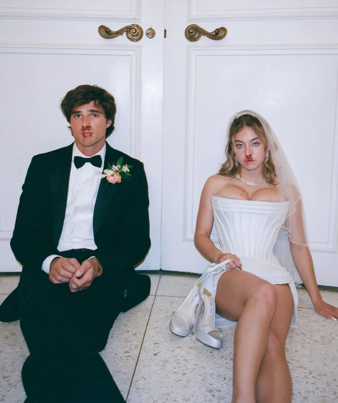 Sydney Sweeney and Jacob Elordi sitting on the floor in wedding attire with bloody noses, possibly for the TV show "Euphoria".