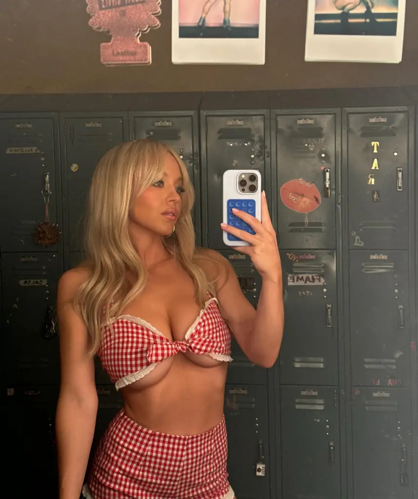 Sydney Sweeney poses for a mirror selfie in a red and white checkered outfit with a tie-front top.
