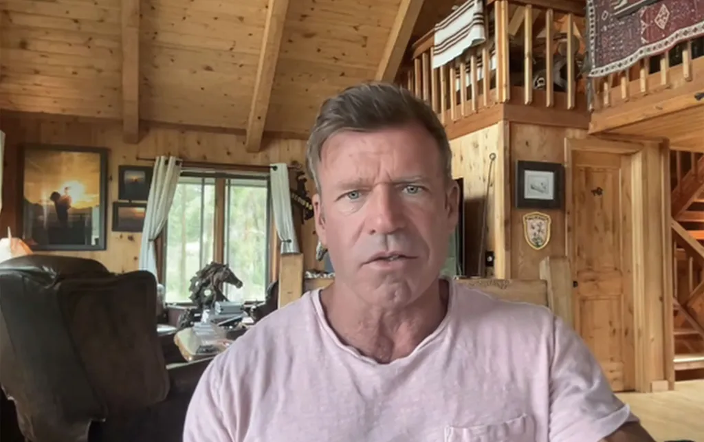 Taylor Sheridan in a pink shirt in a wooden room.