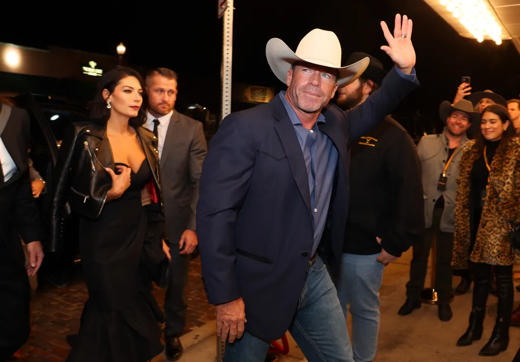 Taylor Sheridan in a white cowboy hat and blue suit jacket, with his wife Nicole Sheridan in a black dress and leather jacket, at the Yellowstone Season 5 premiere.