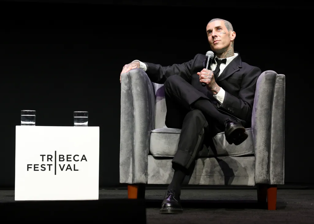 Travis Barker, seated and holding a microphone, speaks at the "Travis Barker: Louder Than Fear" premiere during the 2026 Tribeca Festival.