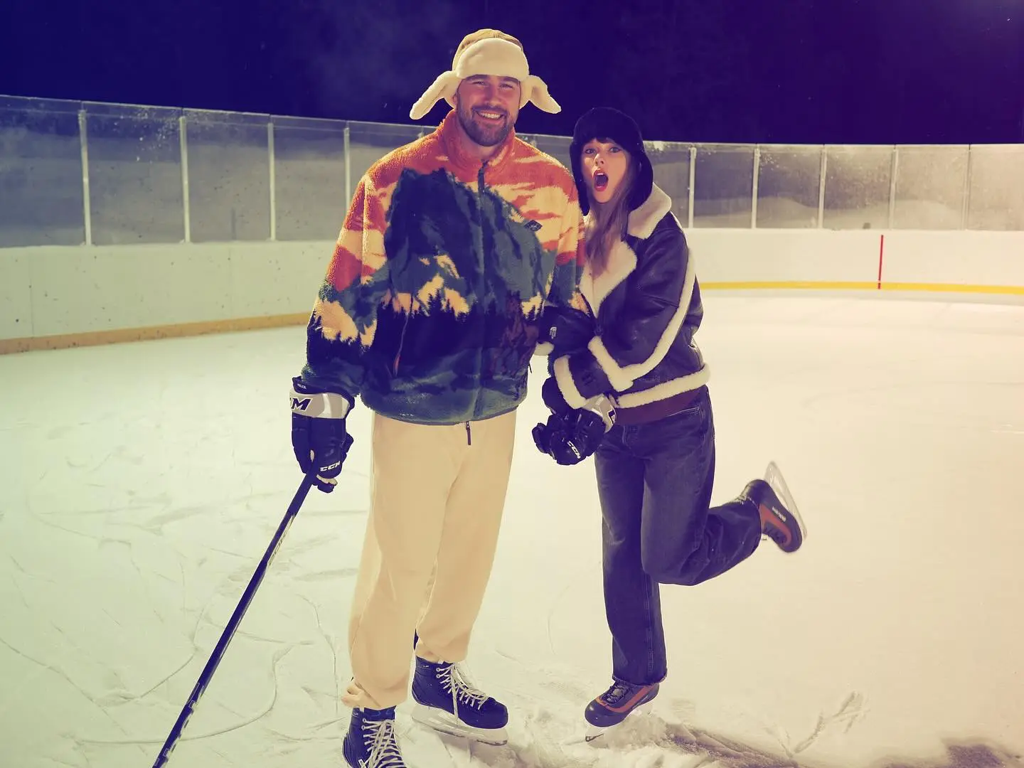 Travis Kelce and Taylor Swift ice skating on a hockey rink.