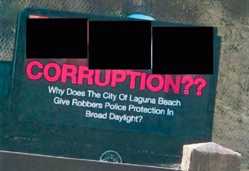 A sign asking, "CORRUPTION?? Why Does The City Of Laguna Beach Give Robbers Police Protection In Broad Daylight?"