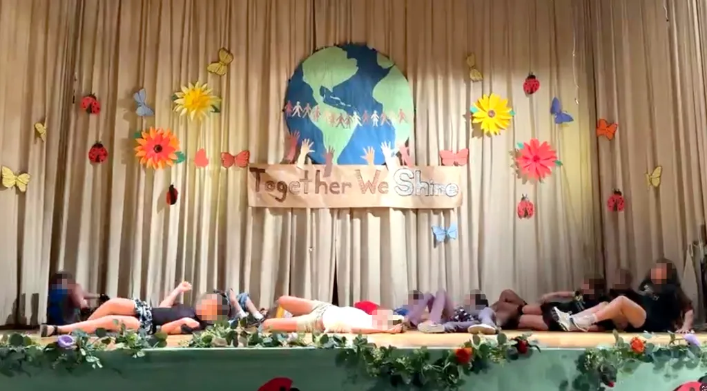 Upper West Side elementary school children lie on the stage in a choreographed dance, with a backdrop of a globe and a banner that reads "Together We Shine."