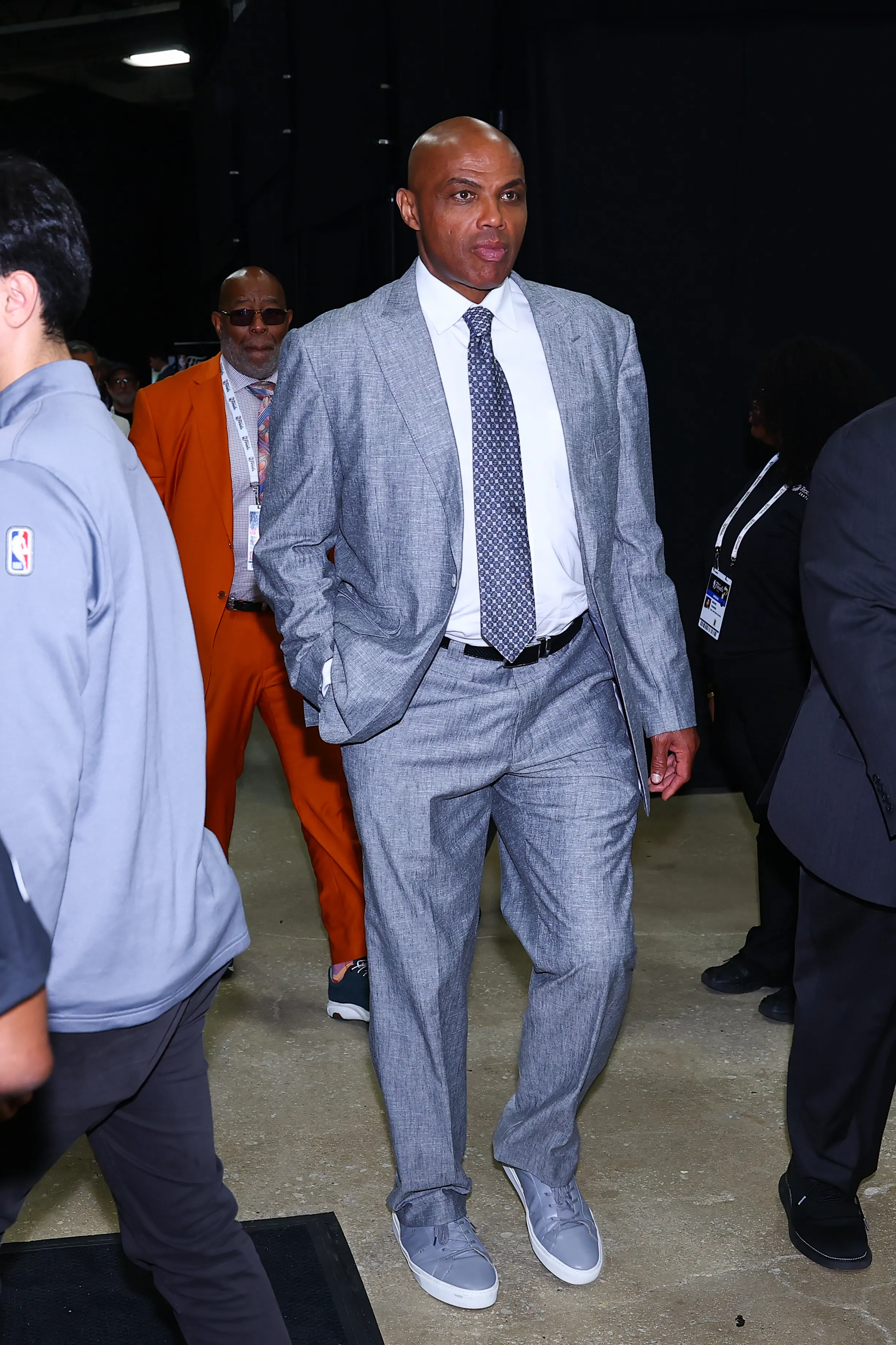 Charles Barkley walks in a gray suit with a patterned tie and gray sneakers.