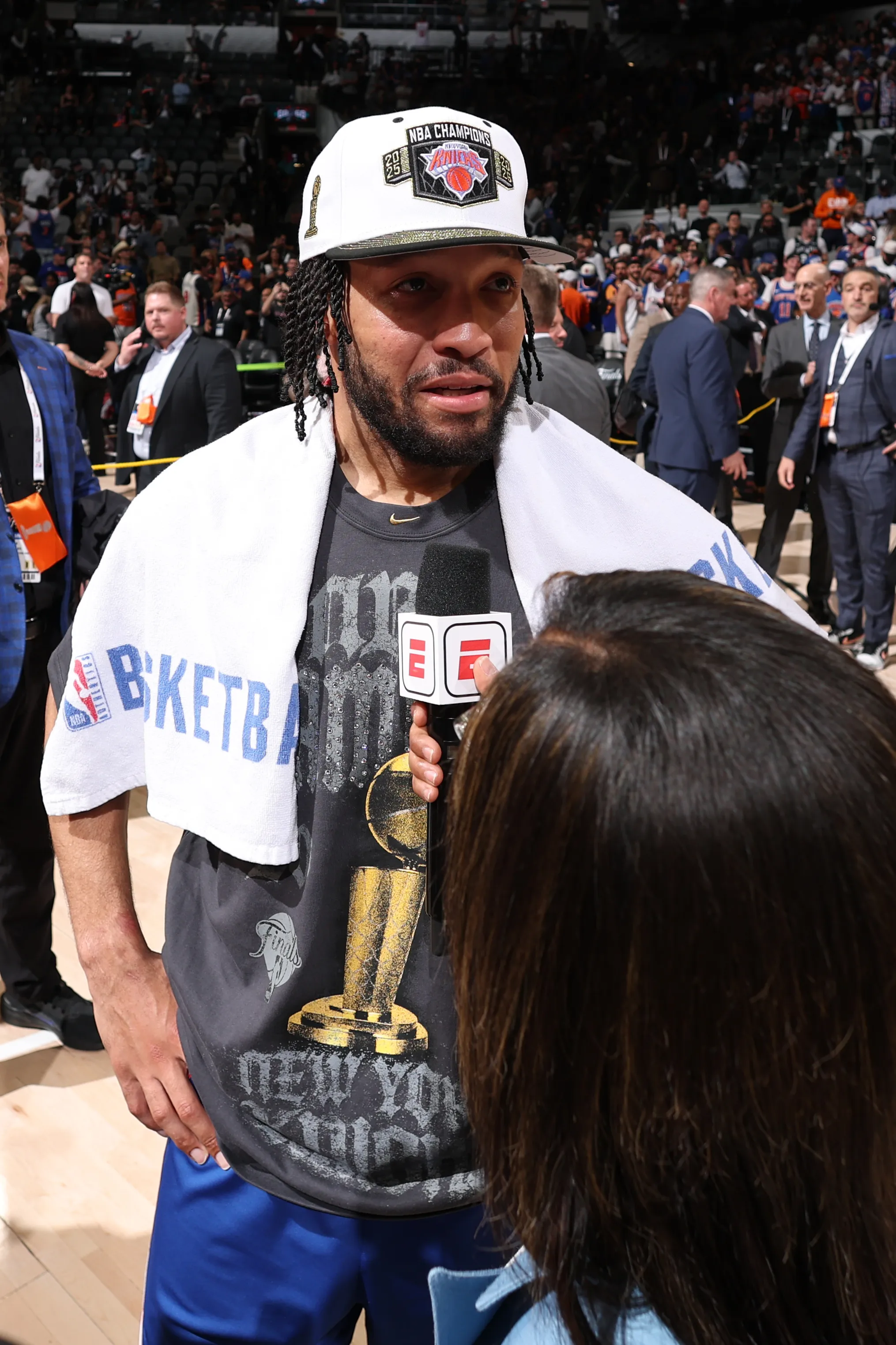 Jalen Brunson wearing an "NBA Champions" hat and a t-shirt with the NBA Finals trophy.