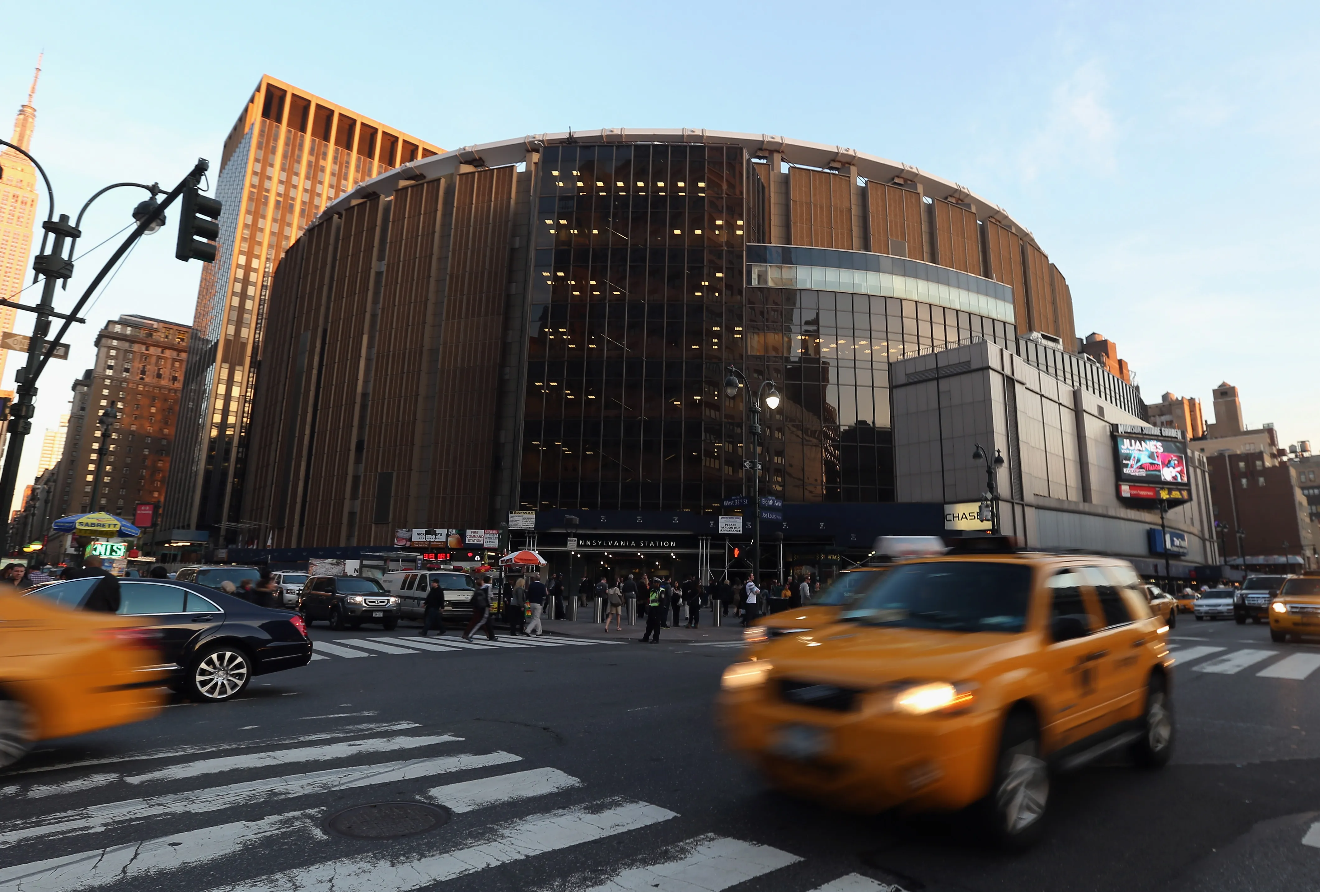 Exterior view of Madison Square Garden with blurred yellow taxis driving on the street in front.