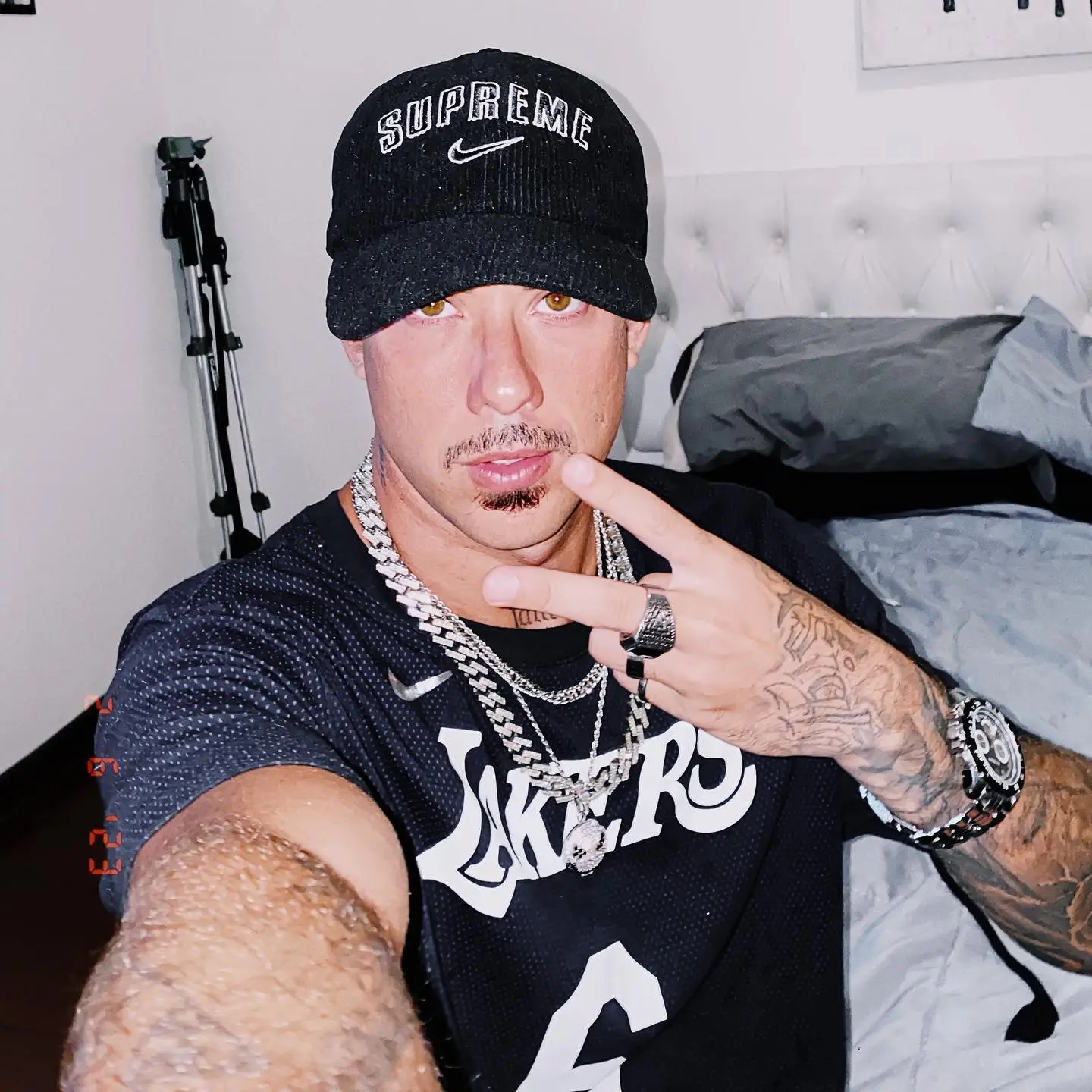 Victor Wao in a black Lakers jersey, Supreme hat, and chain, making a peace sign.