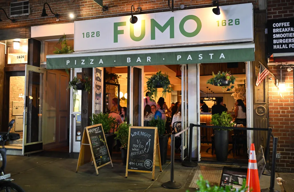 Exterior view of Fumo Upper East Side restaurant with visible diners inside, signage, and menus outside.