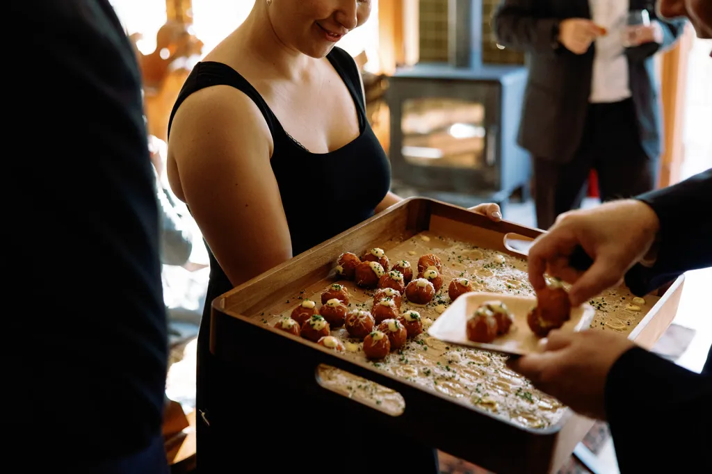 A person holding a tray of crispy arancini with pork ragu, garlic aioli, and parmigiano reggiano cheese, served on small plates.