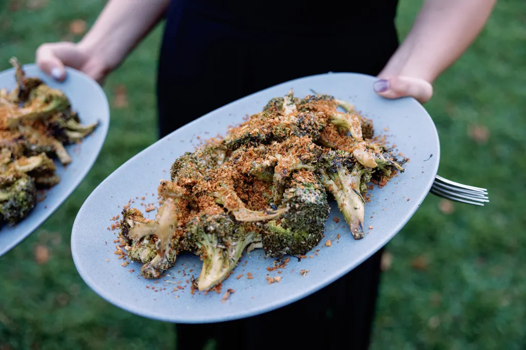 Grilled broccoli with Caesar dressing, lemon zest, and sourdough breadcrumbs, served on light blue plates.