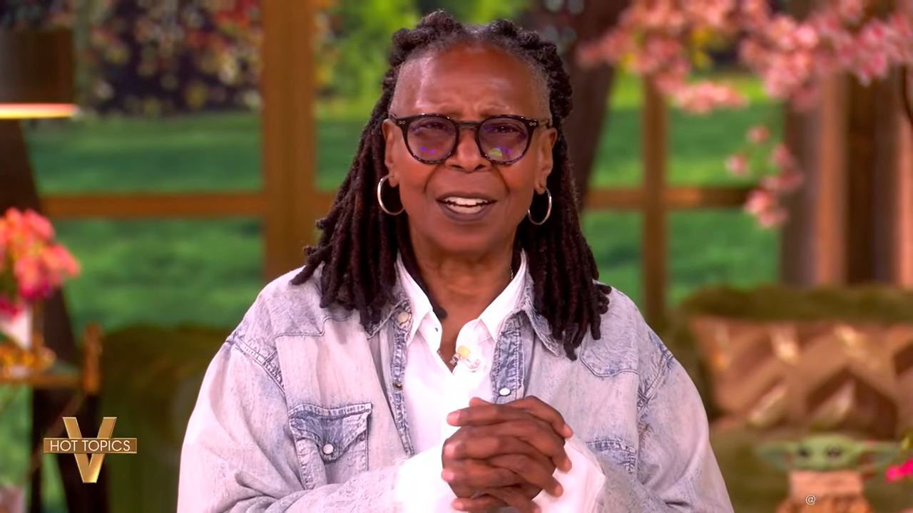Whoopi Goldberg on "The View" holding her cue cards with "Hot Topics" visible on screen.