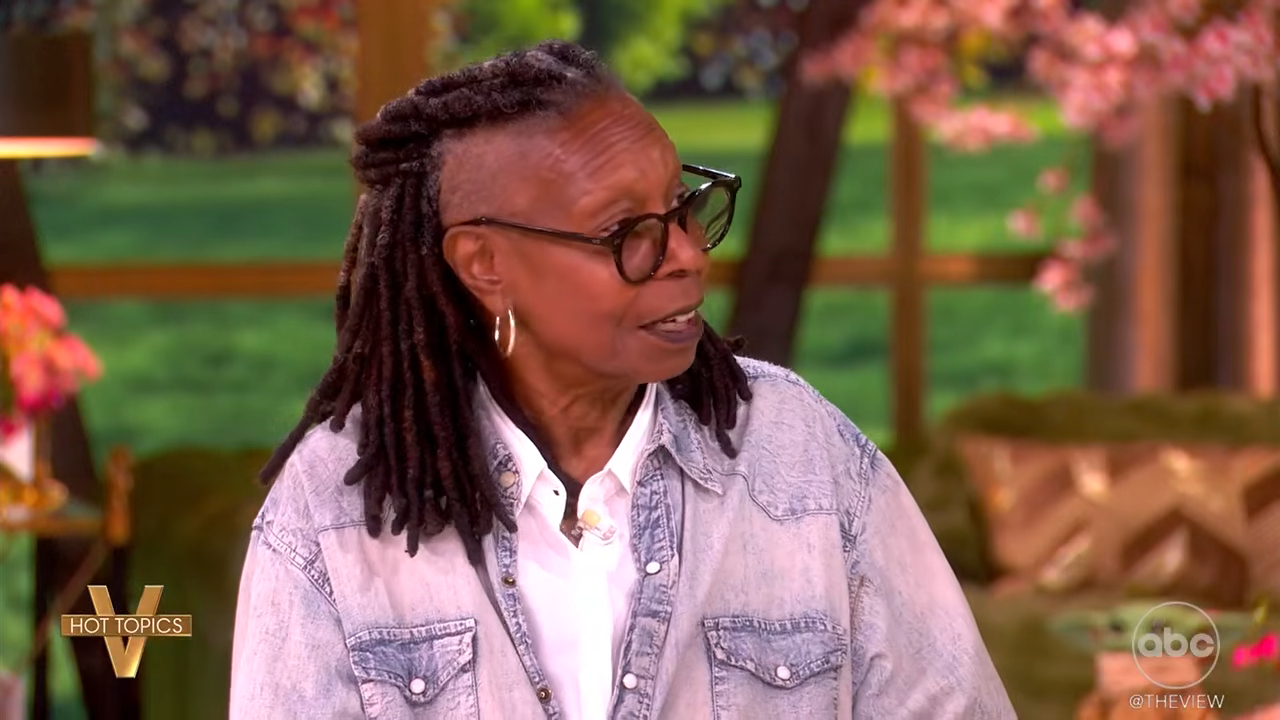 Whoopi Goldberg on "The View" wearing glasses, a denim shirt, and dreadlocks with shaved sides, looking to her right and speaking.