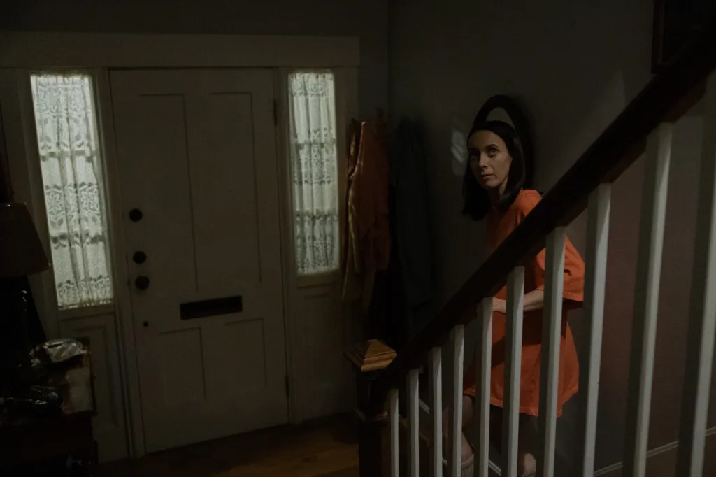 Kate O'Flynn in Widow's Bay, looking back from the middle of a dimly lit staircase.
