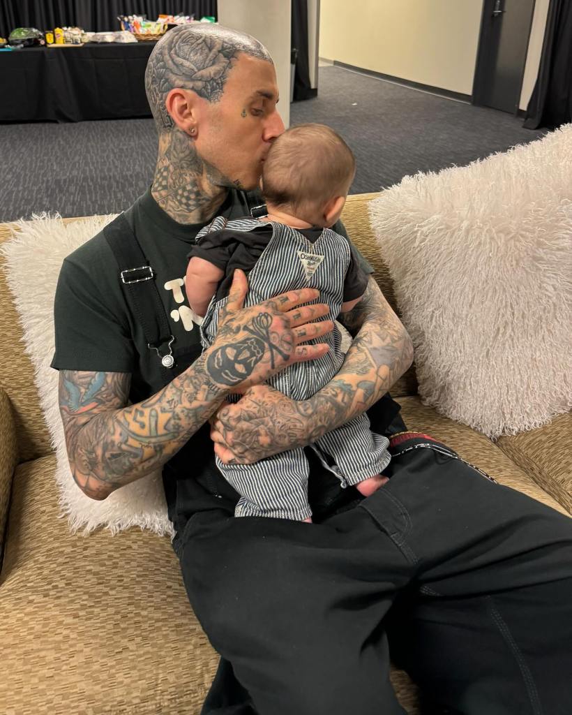 Travis Barker kissing his baby on the head while sitting on a couch.