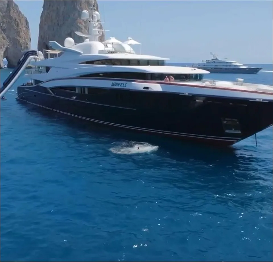 Yacht "Wheels" with a slide into the water and a person swimming near it.