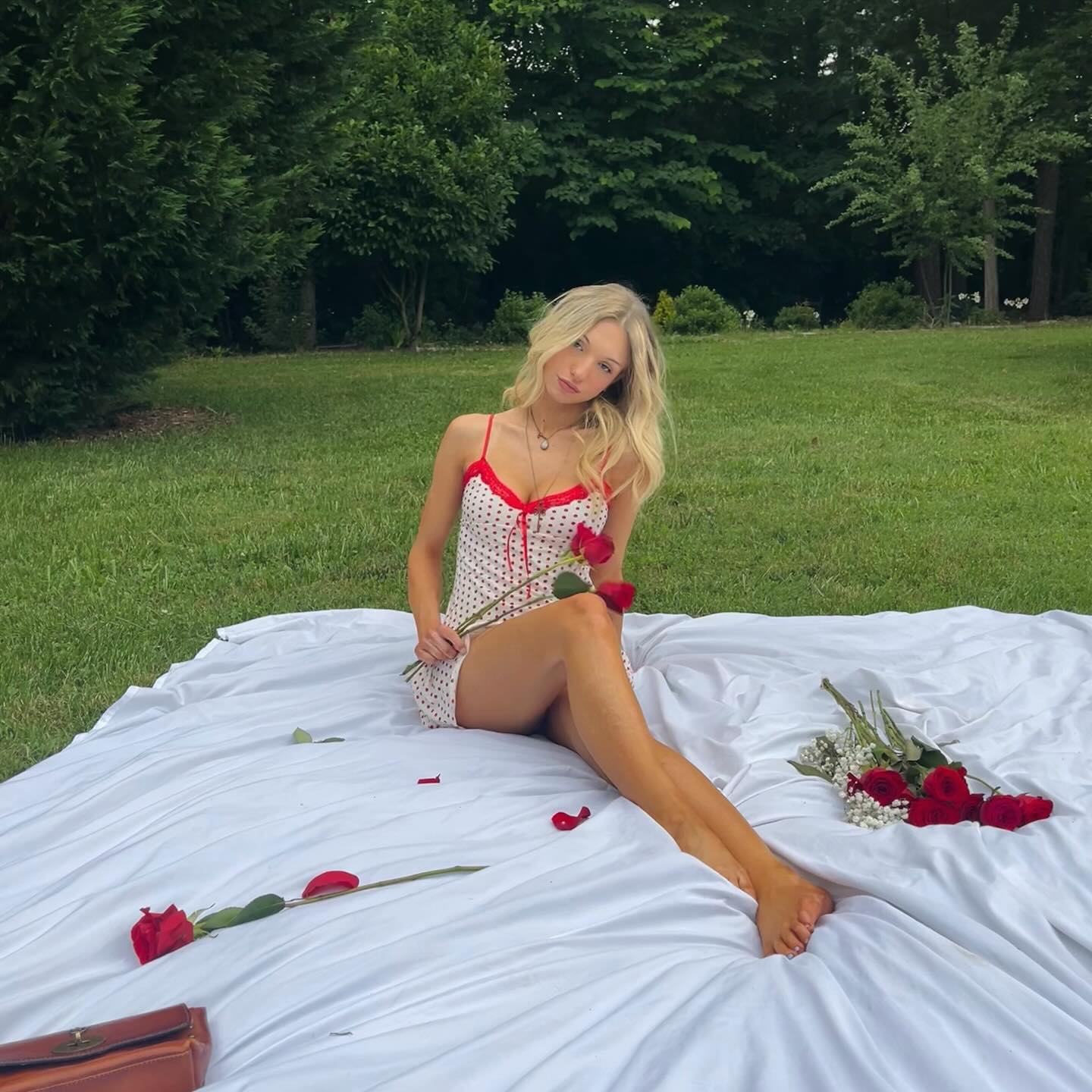 Jordan Meyers wearing a red and white polka dot dress, sitting on a white sheet with red roses.