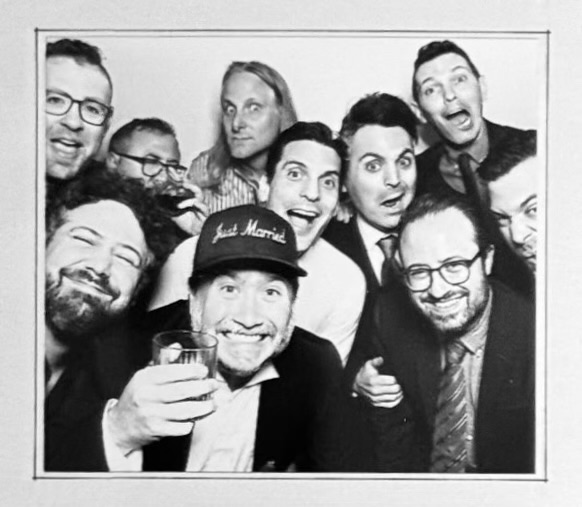 Black and white photo booth picture of the groom, Trent Olsen, in a "Just Married" hat, with several men at his wedding.