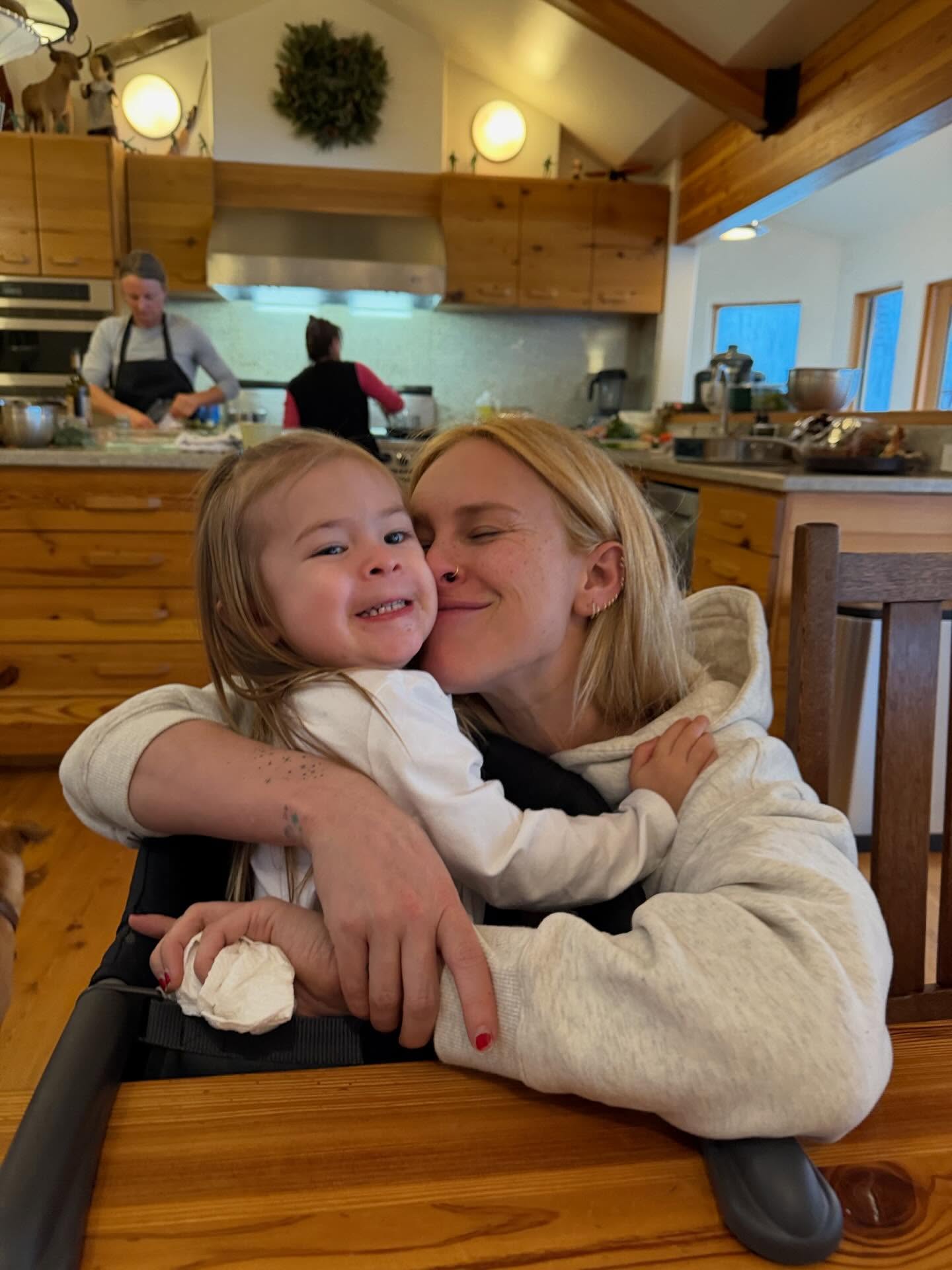 Rumer Willis hugging her child and kissing their cheek in a kitchen.