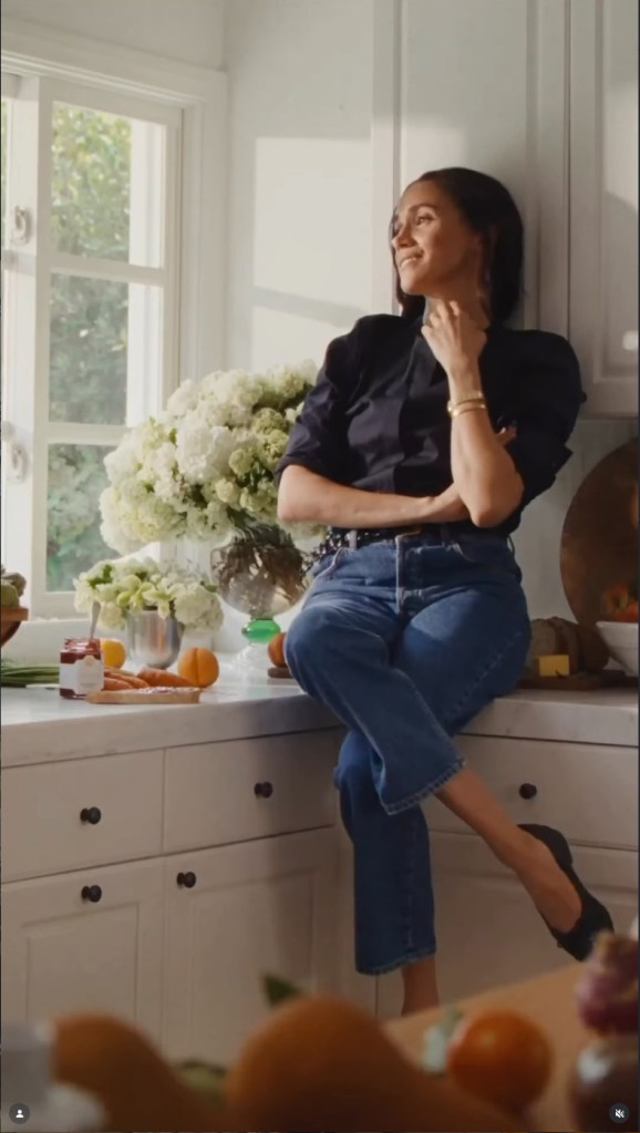 Meghan Markle sitting on a kitchen counter with flowers and fresh produce around her.