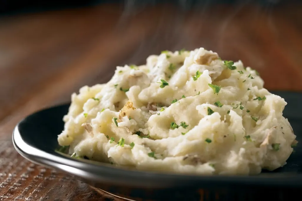 Steaming mashed potatoes with parsley on a black plate.
