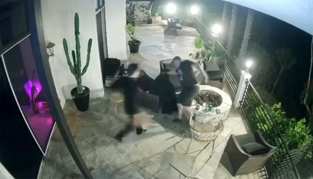 Two men appear to scuffle on a patio next to a fire pit at night.